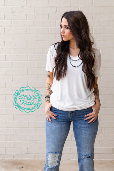 This simple white tee is perfect for any occasion, dressed up or down! With the silky soft material, and the size accommodations, you'll be wearing a smile with it too! This tee has a flattering V-Neck, short sleeves, and a straight hem along the bottom.   Model is wearing a Small but could have sized down to a XS  MSRP: $20+  Perfect Tee. Matches EVERYTHING!!  94% modal, 6% spandex