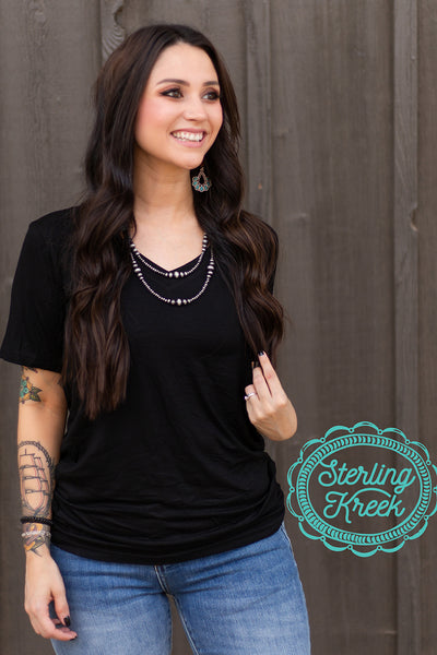 This simple black tee is perfect for any occasion, dressed up or down! With the silky soft material, and the size accommodations, you'll be wearing a smile with it too! This tee has a flattering V-Neck, short sleeves, and a straight hem along the bottom.   Model is wearing a size Small  but could have sized down to an XS  MSRP: $20+  94% modal, 6% spandex